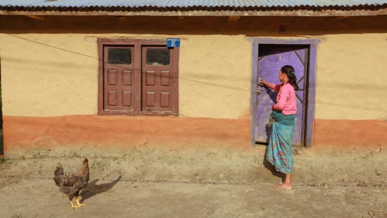 Woman and hen in front of a colorful village house facade.